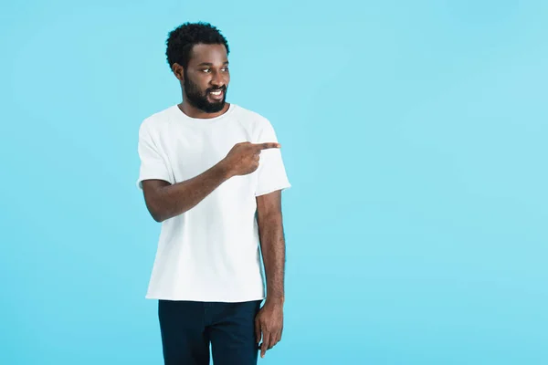 Lächelnder afrikanisch-amerikanischer Mann in weißem T-Shirt, der vereinzelt auf blauem Grund zur Seite zeigt — Stockfoto