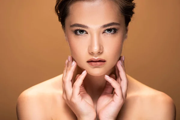 Young beautiful naked woman with shiny makeup looking at camera and touching face isolated on beige — Stock Photo