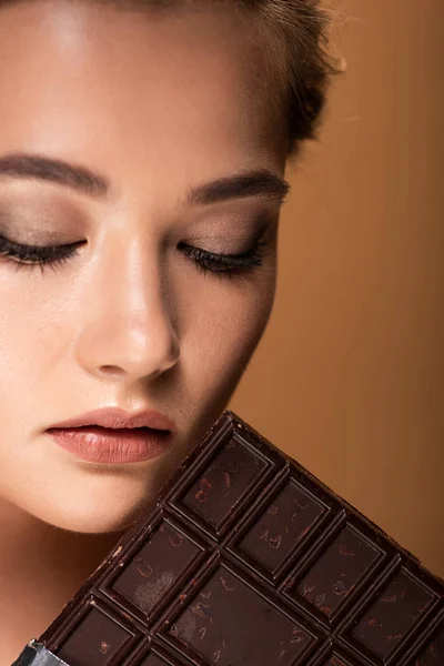 Beautiful young woman with closed eyes holding chocolate bar isolated on beige — Stock Photo