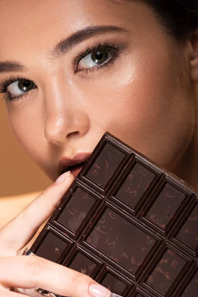Belle jeune femme tenant barre de chocolat isolé sur beige — Photo de stock