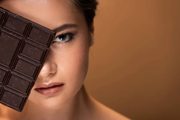 Belle jeune femme au visage obscur tenant barre de chocolat isolé sur beige — Photo de stock