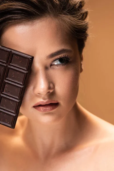 Hermosa mujer desnuda joven con cara oscura sosteniendo barra de chocolate aislado en beige - foto de stock
