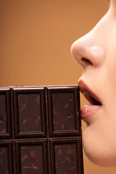 Visão parcial da bela jovem segurando barra de chocolate perto da boca aberta isolada no bege — Fotografia de Stock