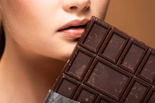 Partial view of beautiful young woman holding chocolate bar isolated on beige — Stock Photo
