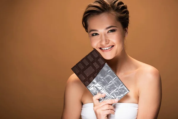 Heureuse belle jeune femme tenant barre de chocolat en feuille d'argent isolé sur beige — Photo de stock