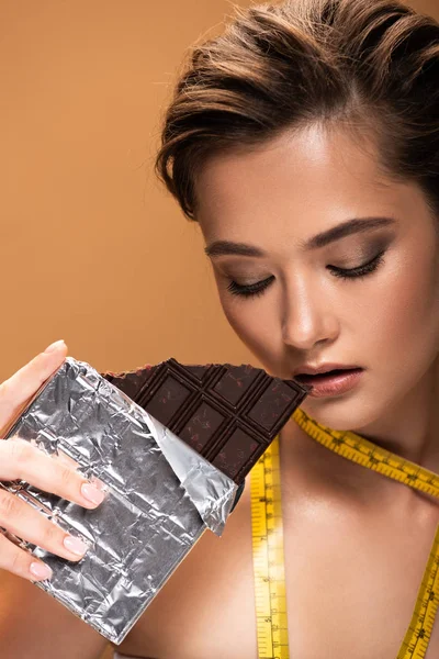 Giovane donna nuda con nastro di misurazione giallo che tiene la barra di cioccolato in lamina d'argento isolata sul beige — Foto stock