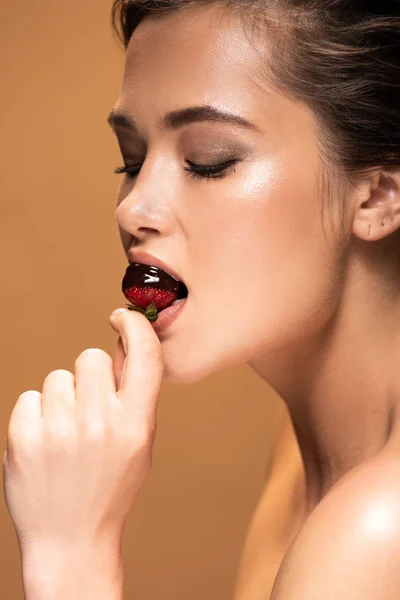 Красива гола жінка з закритими очима їсть полуницю в розтопленому шоколаді ізольована на бежевому — стокове фото