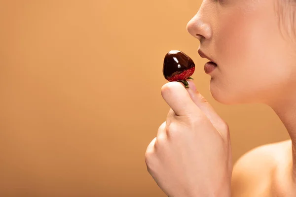 Side view of beautiful naked woman holding strawberry in melted chocolate isolated on beige — Stock Photo