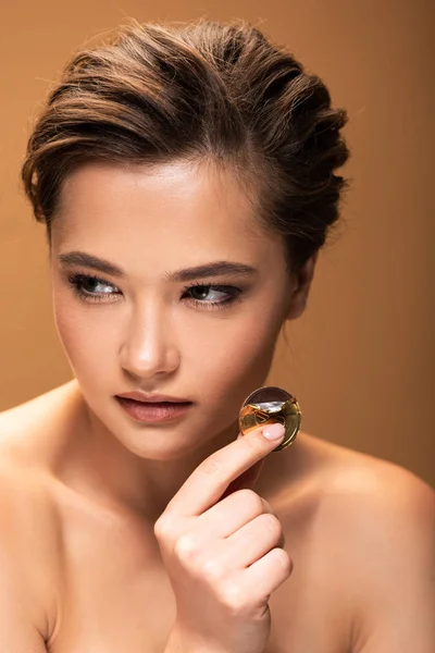 Naked young woman holding chocolate coin in golden foil and looking away isolated on beige — Stock Photo