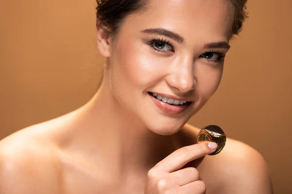 Smiling naked young woman holding chocolate coin in golden foil isolated on beige — Stock Photo