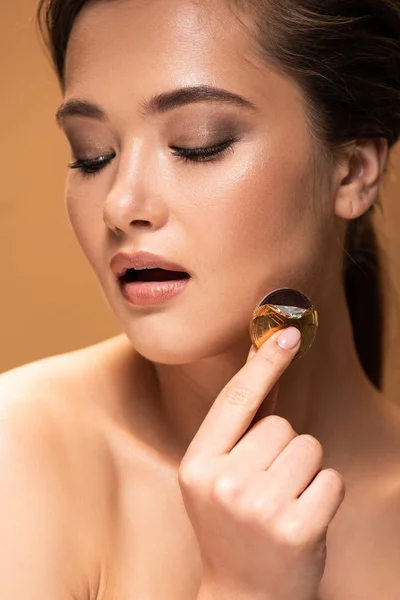 Naked young woman with open mouth holding chocolate coin in golden foil isolated on beige — Stock Photo