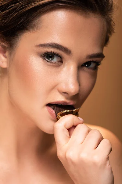 Nua jovem mulher comendo moeda de chocolate em folha dourada isolada no bege — Fotografia de Stock