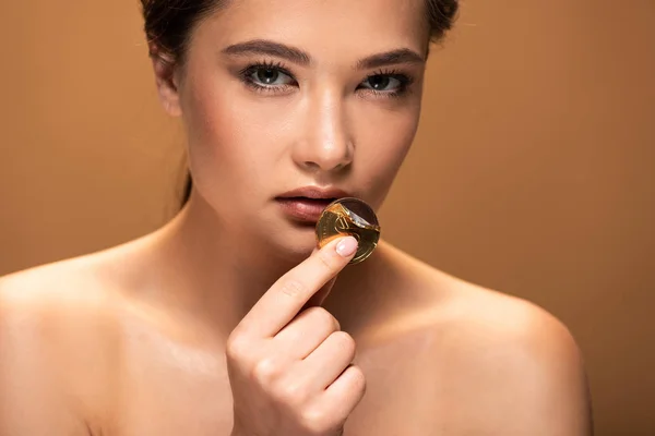 Naked young woman holding chocolate coin in golden foil near lips isolated on beige — Stock Photo