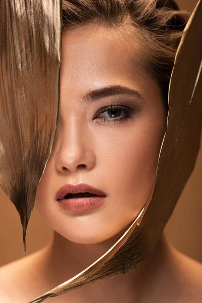 Beautiful young woman with decorative golden leaves looking at camera isolated on beige — Stock Photo