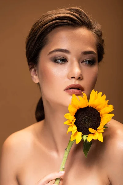Schöne junge nackte Frau mit gelben Sonnenblumen, die isoliert auf braun wegschaut — Stockfoto