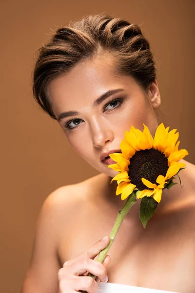 Hermosa mujer desnuda joven con girasol amarillo aislado en marrón - foto de stock
