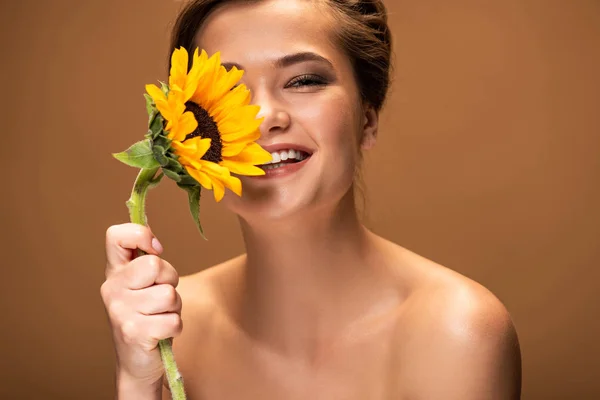 Happy laughing beautiful naked woman with yellow sunflower isolated on brown — Stock Photo