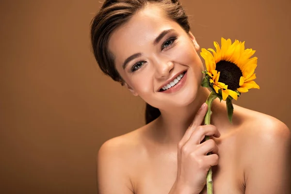 Счастливая красивая молодая голая женщина с желтым подсолнухом изолированы на коричневый — стоковое фото