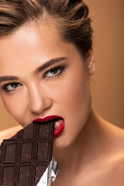 Hermosa mujer con labios rojos mordiendo barra de chocolate en lámina de plata aislado en beige - foto de stock