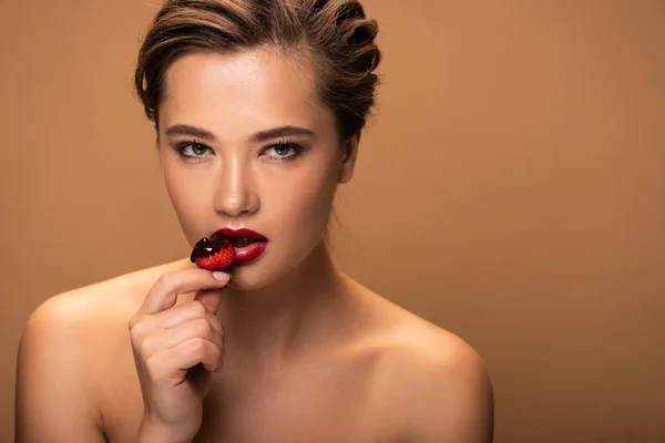 Naked beautiful woman holding strawberry with melted chocolate near lips isolated on beige — Stock Photo