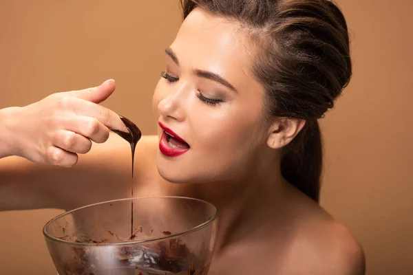Оголена жінка з червоними губами їсть розтоплений шоколад з миски ізольовані на бежевому — стокове фото