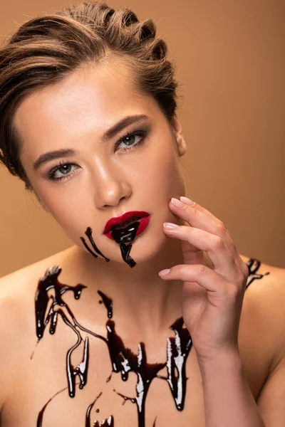 Dirty naked woman with red lips and chocolate spills on skin touching face isolated on beige — Stock Photo