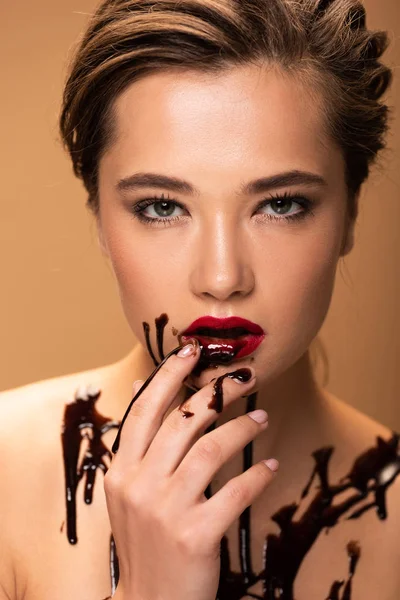 Hermosa mujer desnuda con derrames de chocolate en la piel tocando labios rojos aislados en beige - foto de stock