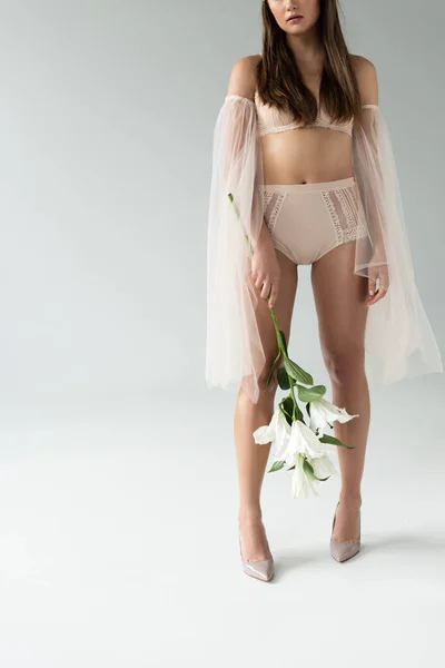 Partial view of tender young woman in beige lingerie and mesh sleeves holding flowers — Stock Photo