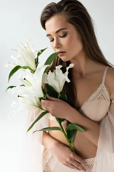 Zarte junge Frau in beiger Dessous hält Lilien isoliert auf weißem Grund — Stockfoto
