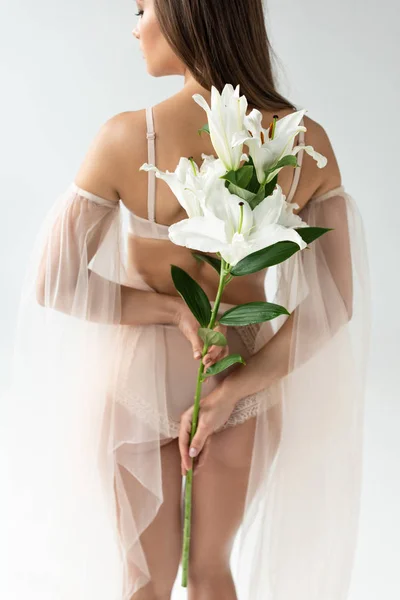 Délicate jeune femme en lingerie beige et manches en mesh tenant bouquet de lis isolé sur blanc — Photo de stock