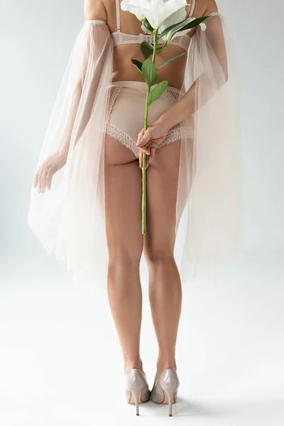 Abgeschnittene Ansicht einer zarten jungen Frau in beiger Dessous und Netzärmeln, die einen Strauß Lilien isoliert auf weißem Grund hält — Stockfoto