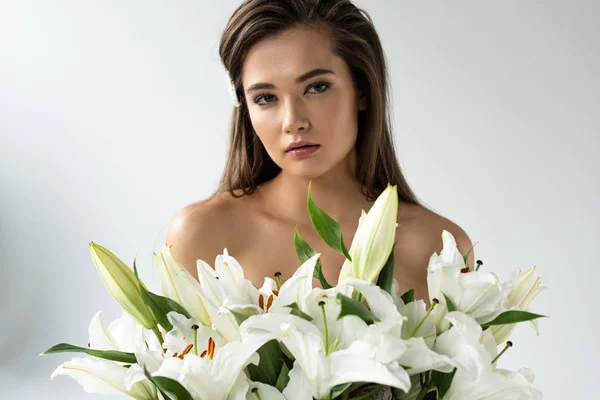 Zarte nackte junge Frau blickt in die Kamera in der Nähe weißer Lilien — Stockfoto