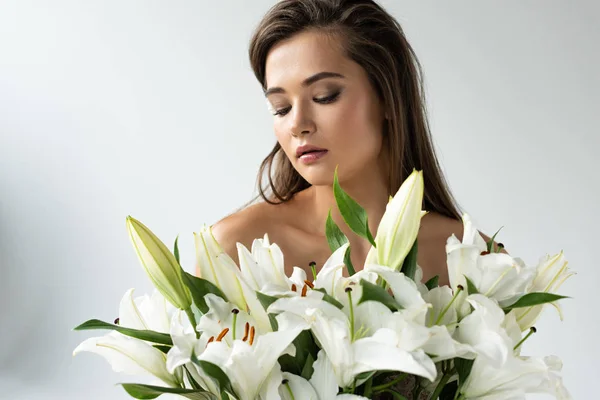 Zarte nackte junge Frau, die in der Nähe weißer Lilien wegschaut — Stockfoto