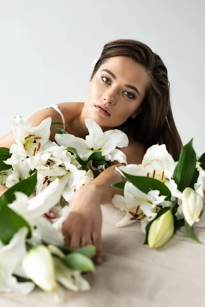 Нежная молодая женщина смотрит на камеру среди лилий, изолированных на белом — стоковое фото