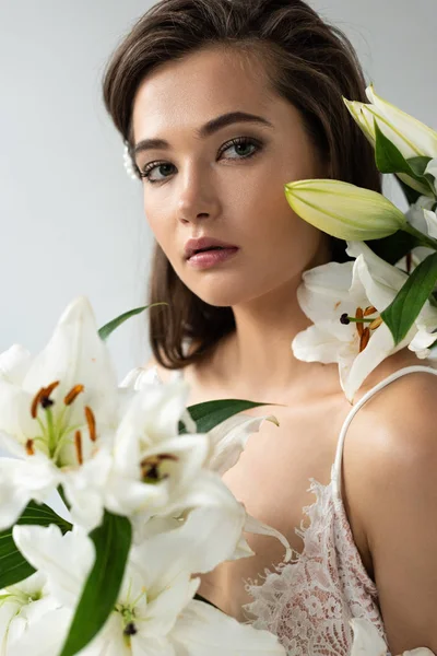 Tender young woman in white lacy bodysuit among lilies isolated on white — Stock Photo