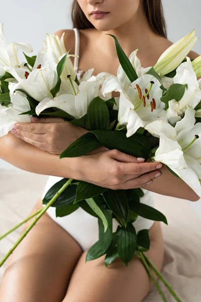 Ausgeschnittene Ansicht einer zarten jungen Frau im weißen Spitzenbody mit Lilienstrauß auf weißem Hintergrund — Stockfoto