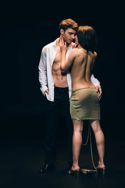 Donna svestita con glutei sexy in piedi vicino elegante fidanzato con busto nudo isolato su nero — Foto stock