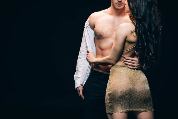 Cropped view of sexy brunette woman undressing boyfriend with muscular torso isolated on black with copy space — Stock Photo
