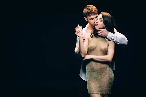 Passionate man touching woman throat while sexy girl in transparent dress holding bottle with perfume isolated on black with copy space — Stock Photo