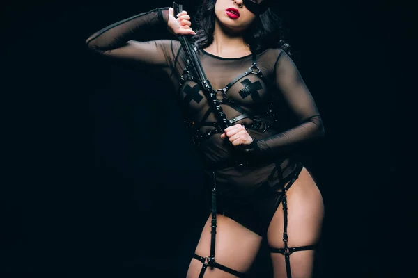 Recortado vista de apasionado caliente morena mujer en bdsm traje con azotes látigo aislado en negro - foto de stock