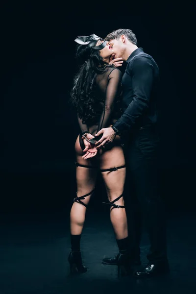 Hombre besos sexy mujer en esposas y sexy bdsm traje en negro fondo - foto de stock