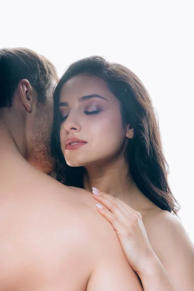 Morena joven con los ojos cerrados abrazando novio desnudo aislado en blanco - foto de stock