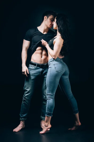 Barefoot couple in denim undressing and kissing isolated on black — Stock Photo