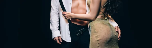 Cropped view of man touching girlfriend buttocks while woman touching belt isolated on black, panoramic shot — Stock Photo