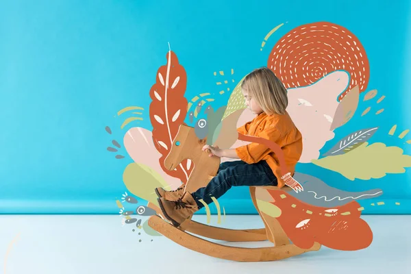 Kid in jeans and orange shirt riding rocking horse on blue background with fairy nature illustration — Stock Photo