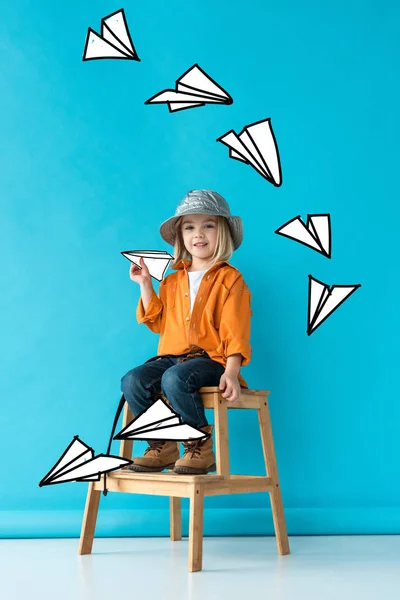 Niño en jeans y camisa naranja sentado en las escaleras y jugando con aviones de papel de hadas - foto de stock