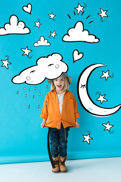 Bambino eccitato in cappello d'argento, jeans e camicia arancione su sfondo blu con stelle, luna, nuvole e illustrazione fata della pioggia — Foto stock