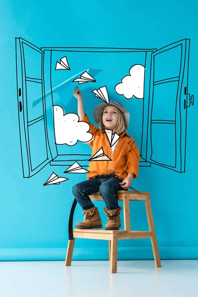 Enfant excité en jeans et chemise orange assis sur les escaliers et jouer avec avion en papier bleu sur fond bleu avec fenêtre blanche fée, avions en papier et nuages illustration — Photo de stock