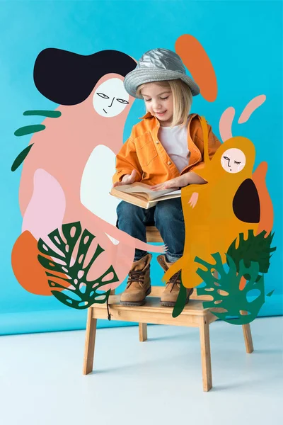 Kid in jeans and orange shirt sitting on stairs and reading book on blue background with fairy characters illustration — Stock Photo