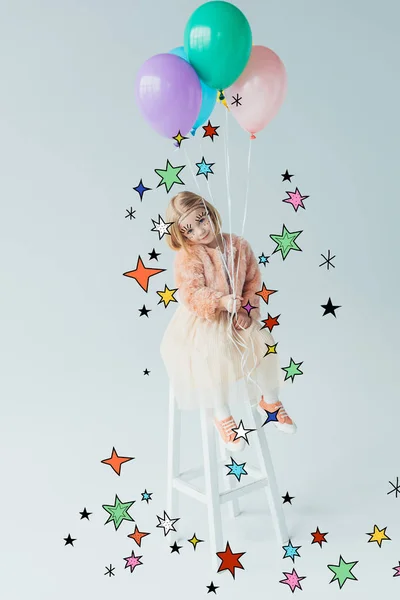 Милый ребенок в искусственном шубе и юбке сидит на стульчике, смотрит в камеру и держит воздушные шары среди звезд — стоковое фото